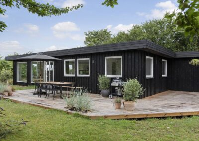 Udvendigt billede af et sommerhus i sort træ med stor træterrasse, spiseplads og grøn have, fotograferet til markedsføring af fritidsbolig i Vestsjælland
