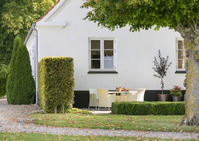 Terrasse ved helårsbolig med spiseplads, velplejet have og klassisk hvid facade, fotograferet til boligmarkedsføring i Danmark