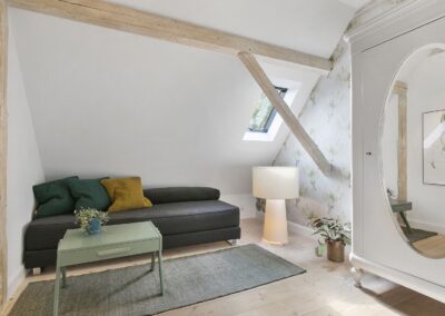 Opholdsrum på tagetage med synlige bjælker, sofa og ovenlysvindue, fotograferet til boligpræsentation i Vestsjælland