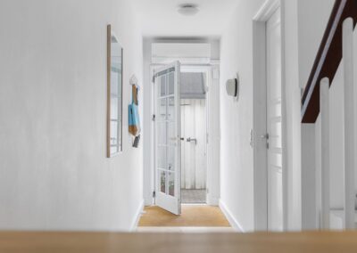 Entré i sommerhus med hvidmalede vægge, glasdør mod terrasse og enkel indretning, fotograferet til sommerhusmarkedsføring i Vestsjælland