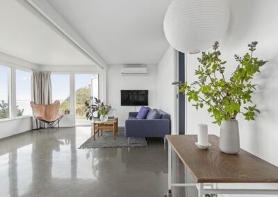Lys stue i helårsbolig eller sommerhus med store vinduespartier, sofaarrangement og udsigt mod vand, fotograferet til eksklusiv boligpræsentation i Danmark